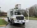 A 2015 Ford F750 bucket truck with a white body and elevated platform for electrical work parked on a roadway