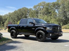 A black 2014 Dodge Ram 1500 pickup truck with a shiny finish and large black wheels parked on a driveway