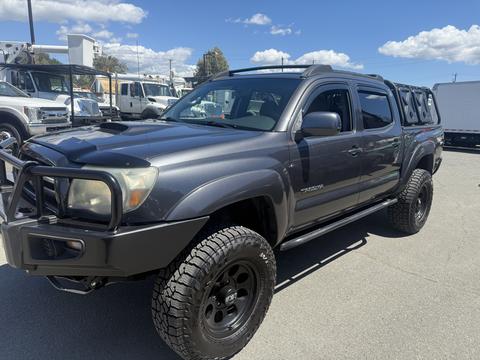 A gray 2010 Toyota Tacoma with off-road tires and a black grill guard parked at a dealership