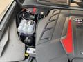 The image shows the engine bay of a 2020 Audi RS with a prominently displayed engine cover featuring a red and black design and various mechanical components and fluid reservoirs