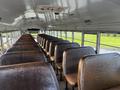 Interior of a 2005 Blue Bird 48 passenger bus featuring rows of brown leather seats and metal railings on the sides