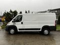 A 2018 RAM Promaster van in white with a black lower section parked on a wet surface showcasing its side profile and large cargo area