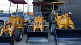 Three compact construction machines with yellow bodies and front loaders, labeled Fland and Traner, lined up for display in a work yard