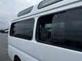 A white 2002 Nissan Van featuring large windows and a high roof design with visible water droplets on the glass