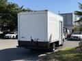 A white 2013 Isuzu NPR box truck parked with its rear facing the viewer and a blank back panel