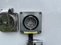 A gray power inlet with a circular connector and three prongs mounted on a white surface