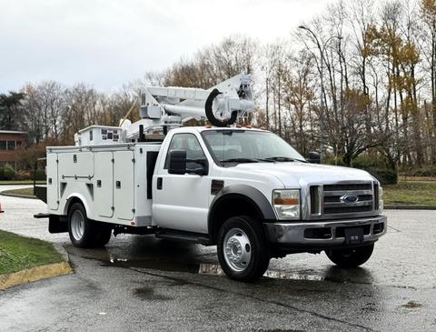 A white 2008 Ford F-550 with a bucket truck mounted on top and a utility box on the side is parked on a wet surface
