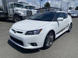 A white 2013 Scion TC with a sleek design and sporty features, showcasing alloy wheels and distinctive side decals