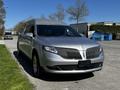A silver 2013 Lincoln MKT with a distinctive grille parked on a street with a clear sky and trees in the background