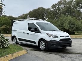A white 2018 Ford Transit Connect van with a black front and a roof rack parked on a street