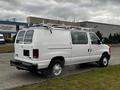 A white 2011 Ford Econoline van with a roof rack and sliding side door is parked, with smoke visible coming from the rear exhaust