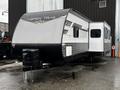 A 2022 Aspen Trail travel trailer with a sleek design featuring a silver and black exterior and an extended section on the side