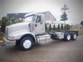 A silver 2013 International 5900i truck with a prominent cab and a flatbed chassis is parked on an asphalt surface