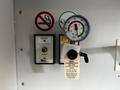 A gauge next to an oxygen button and a sign indicating no smoking with instructions for a Rico combination valve labeled for on-off and regulating value