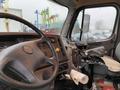 The interior of a 2020 Freightliner 114SD truck featuring a steering wheel dashboard controls and a gear shifter with paper rolls on the seat and floor