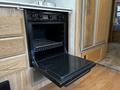 A black oven with a pull-out door and a wire rack inside set within the cabinetry of a 2000 Ford Motorhome