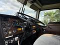 The interior of a 1996 Kenworth T800 featuring a large steering wheel numerous gauges and controls with a fabric seat in the foreground