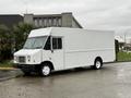 A white 2018 Ford E-450 cargo van with a boxy design and large front windows parked on a wet surface