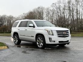 A 2016 Cadillac Escalade in white with chrome accents and large alloy wheels parked on a wet surface