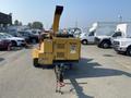 A yellow 2010 Vermeer Corporation BC1200XL wood chipper with a rear chute and towing hitch positioned in a parking lot surrounded by vehicles