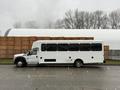 A white 2011 Ford F-550 bus with large windows and a boxy shape parked on a street