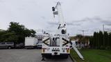 A white 2012 International 7400 truck with a raised crane arm and a bucket attached on top for lifting purposes