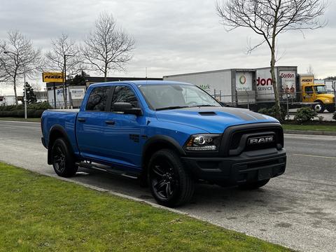 A blue 2021 RAM 1500 Classic pickup truck with a black grille and accents parked on the side of a road