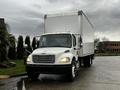 A white 2018 Freightliner M2 106 box truck parked with its headlights on and a blank cargo area in the back