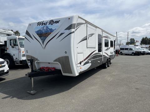 A white 2013 Outdoor Wind River travel trailer with a distinctive mountain design at the front and a hitch attachment visible at the bottom