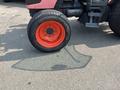 A close-up of a 2010 Kubota M6040 tractor tire with an orange rim and a thick tread pattern casting a shadow on the ground