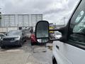 A white 2017 Ford Econoline van is parked with its side mirror prominently visible, reflecting nearby vehicles and a cloudy sky