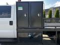 A 2016 Ford F-550 with dual black storage compartments mounted on the side of its flatbed, featuring secured doors and a lower drawer compartment
