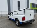 A white 2016 RAM 1500 with a blue stripe and a truck cap in the bed parked at an industrial location
