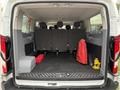 A 2017 Ford Transit van with the rear doors open showcasing an empty cargo area featuring grey seats on one side and a red bag and toolbox on the floor