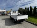 A white 2004 Toyota Toyoace truck with a flatbed is parked, facing away from the viewer, showcasing its rear and side profile