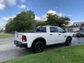 A white 2021 RAM 1500 truck with black wheels parked on a grassy area showing its rear and side profile