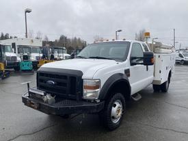 A 2009 Ford F-350 SD Service Truck with a white exterior, front cowling, and utility body equipped with tools and equipment on the side