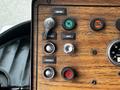 Close-up of a control panel featuring buttons for ignition, lights, starter 1 and 2, and a low air warning light, all set against a wooden background
