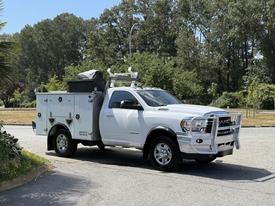A white 2020 Ram 2500 truck with a custom utility body and tool boxes on the back equipped with a ladder rack and chrome bumpers on a sunny day