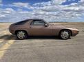 A 1983 Porsche 928 in a soft pink color showing its sleek profile with distinctive wheels and an elongated body design
