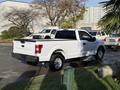 A white 2018 Ford F-150 pickup truck is parked with its bed facing the viewer showcasing its sleek design and modern features