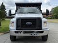A 2017 Ford F-750 truck with a large front grille and chrome bumper is facing the camera with its headlights on and a flatbed designed for carrying heavy loads
