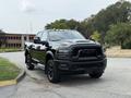 A black 2024 RAM 2500 truck is parked, showcasing a bold front grille, high ground clearance, and rugged tires suitable for off-road driving