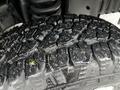 Close-up of a rugged tire featuring a deep tread pattern with some dirt and moisture visible on the surface