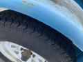 Close-up of a tire on a blue 2003 U-Built Reel Trailer showing a textured tread pattern and a white wheel with rusted bolts