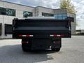 A 2015 Mitsubishi Fuso FE truck viewed from the rear with a black dump bed and red reflectors on the sides