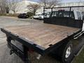 A 2017 GMC Sierra 3500HD with a flatbed in the foreground featuring a wooden surface and metal fencing along the sides