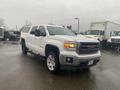 A white 2015 GMC Sierra 1500 with a chrome grille and alloy wheels parked at an angle featuring an extended cab and a truck bed cap