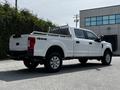 A white 2017 Ford F-250 SD pickup truck with a silver bed rack and four-wheel drive badges parked on a gravel surface