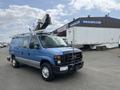 A blue 2010 Ford Econoline van with a ladder and equipment on the roof, parked in a lot with a trailer nearby